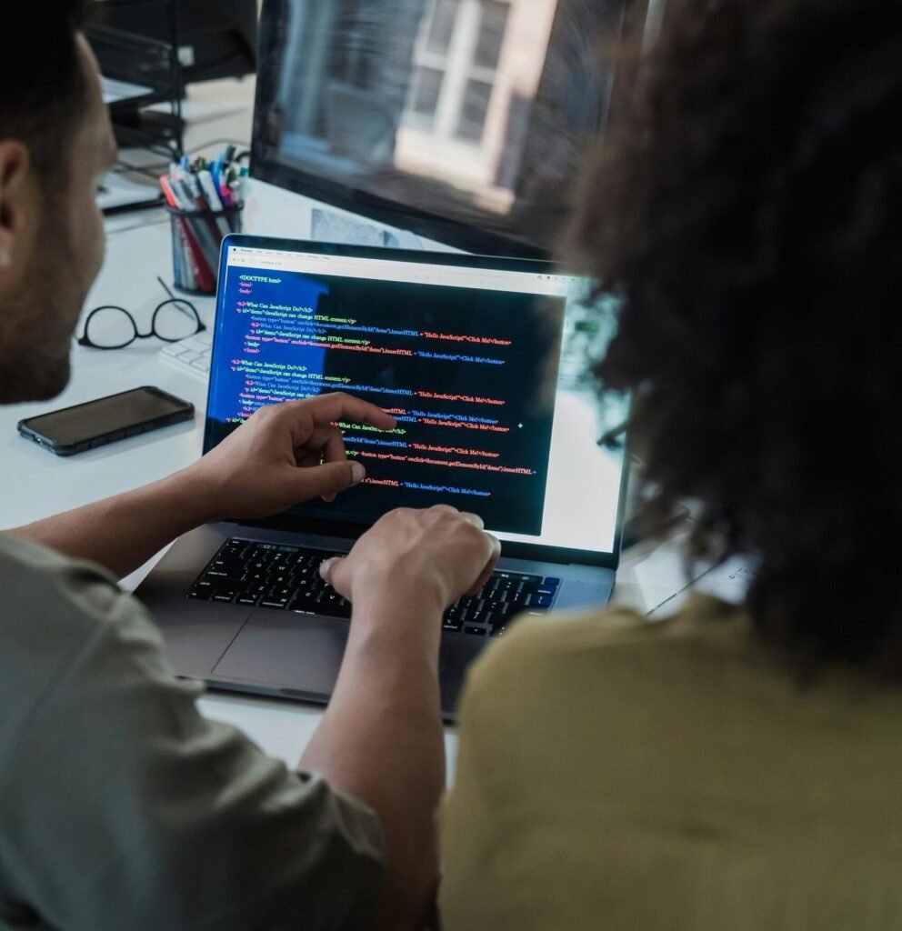 Two adults collaborating on programming tasks using a laptop in an office setting.